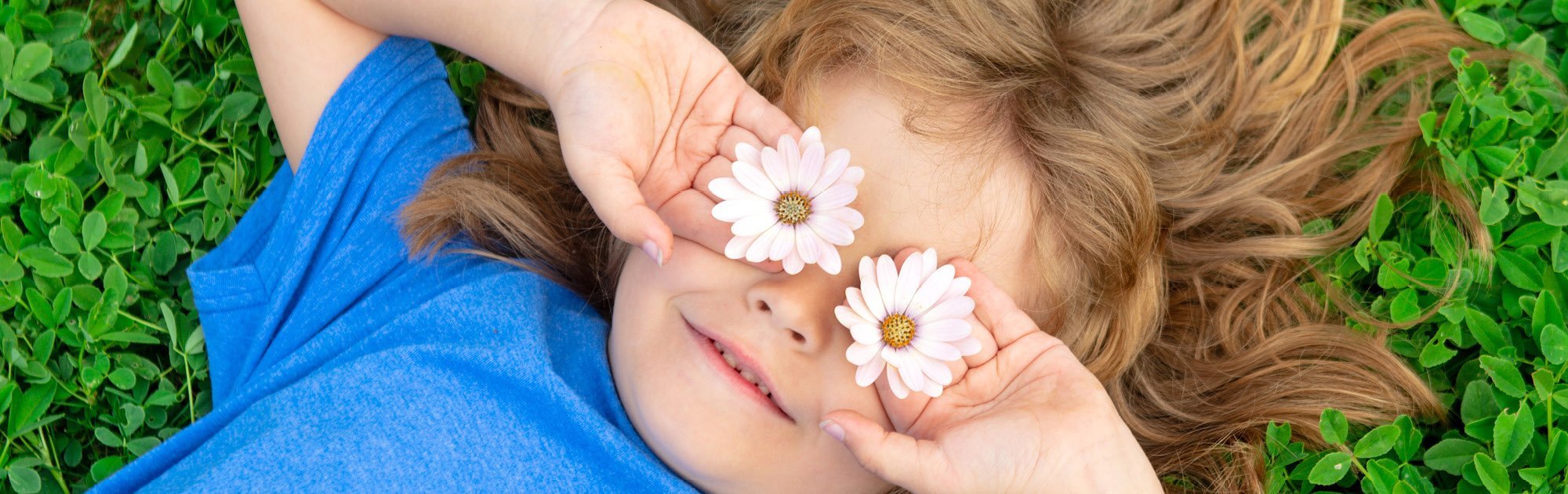 Slider Kinder Kind liegt im Gras und hält zwei Gänseblümchen vor die Augen