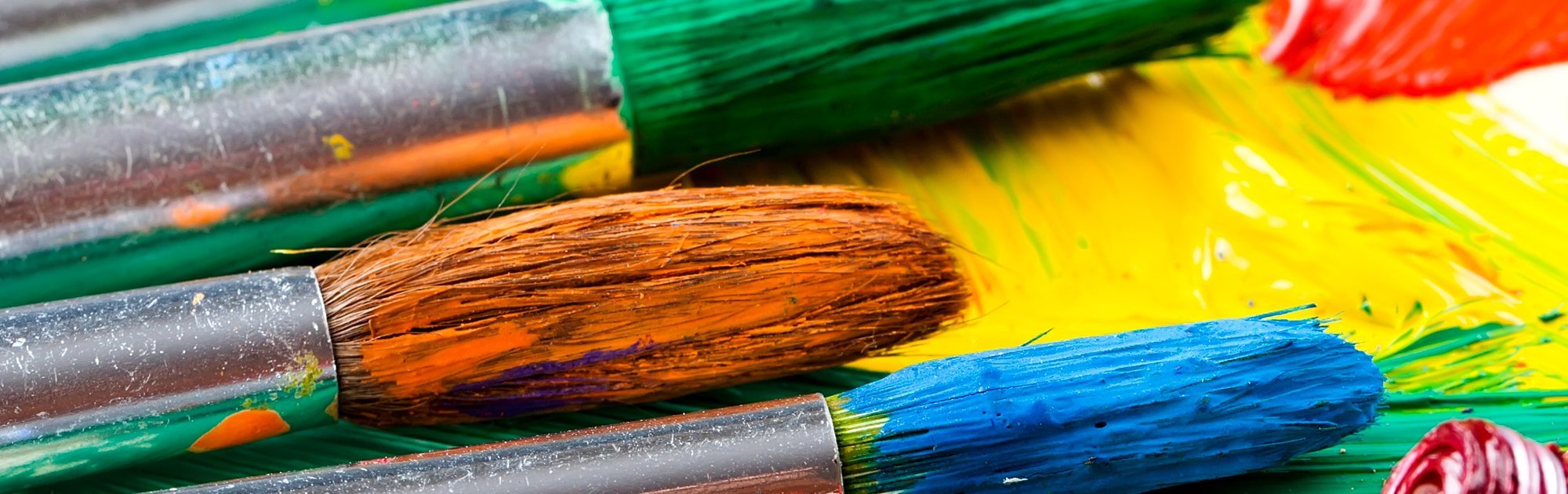 Slider Kreativität Bunte Pinsel liegen auf einer Palette mit verstrichener Farbe in kräftigen Tönen