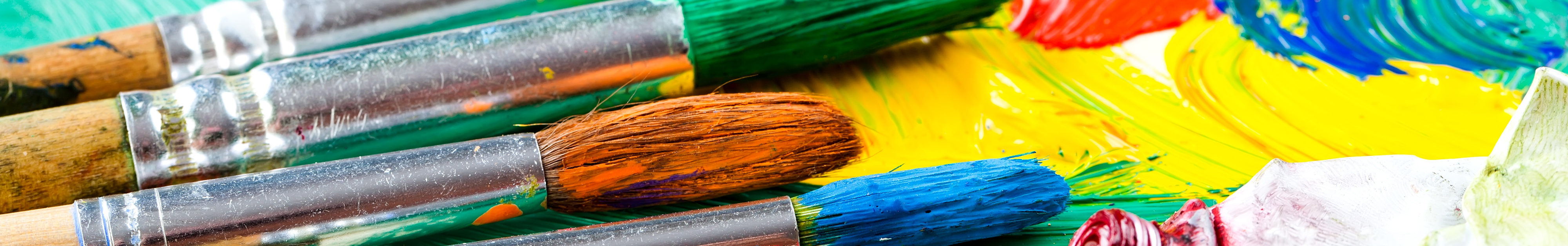 Slider Kreativität Bunte Pinsel liegen auf einer Palette mit verstrichener Farbe in kräftigen Tönen